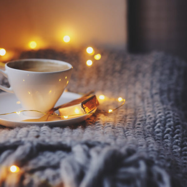 cozy winter or autumn morning at home. Hot coffee with gold metallic spoon, warm blanket, garland and candle lights, swedish hygge concept.